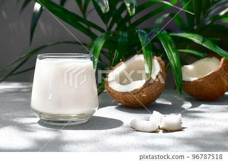 Coconut milk in glass and half of coconut on palm leaf background. Vegetable milk, lactose free non dairy healthy drink. Vegan food. 96787518
