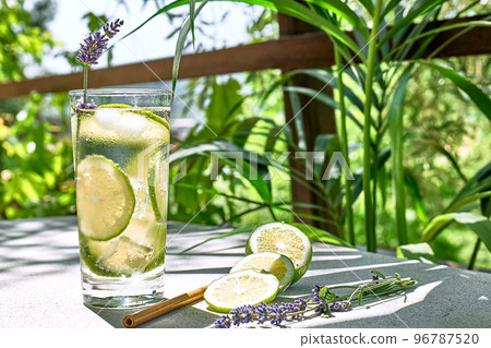 Cool lavender lemonade with lime slices and lavender flower on the table in tropical garden with palm. Healthy organic summer soda drink. Detox water. Diet unalcolic coctail. 96787520