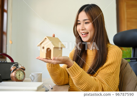 A beautiful Asian female putting a house model on her hands. Real estate agent, home buyer concept. A beautiful Asian female putting a house model on her hands. Real estate agent, home buyer concept. 96787590