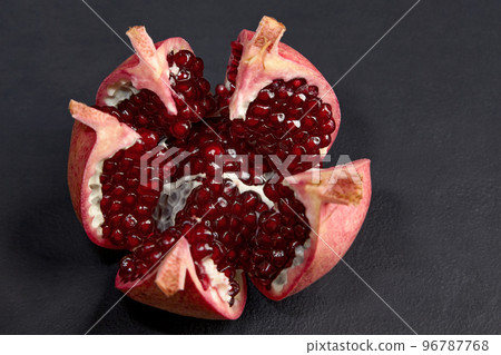 Beautifully cut and broken ripe pomegranate, on a dark concrete background Beautifully cut and broken ripe pomegranate, on a dark concrete background 96787768