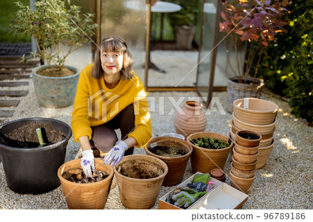 Woman planting flowers in jugs at garden Woman planting flowers in jugs at garden 96789186