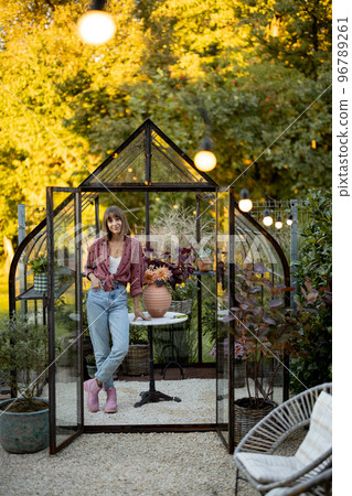 Woman near greenhouse with flowers at back yard 96789261