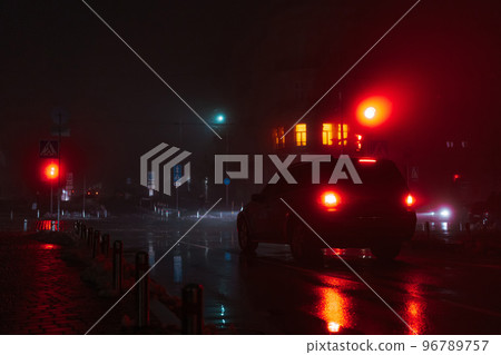 Night foggy street in the city. The car stops at a red traffic light. Soft focus. Night foggy street in the city. The car stops at a red traffic light. Soft focus. 96789757