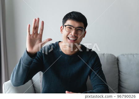 Portrait of young Asian man wearing eye glasses big smiling and looking at camera with feeling happy and positive in living room at home, meeting, video conference. Portrait of young Asian man wearing eye glasses big smiling and looking at camera with feeling happy and positive in living room at home, meeting, video conference. 96790026