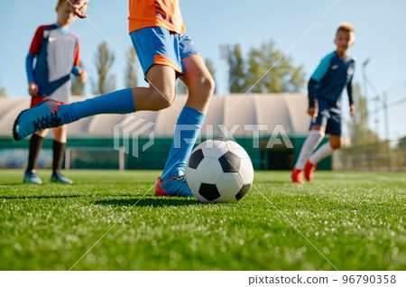 Closeup boy kicking ball while playing football with teammates 96790358