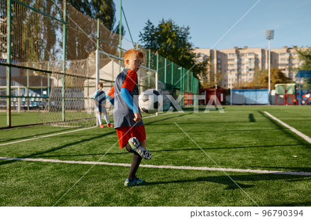 Kids playing soccer game, young boy footballer wearing uniform hitting ball Kids playing soccer game, young boy footballer wearing uniform hitting ball 96790394