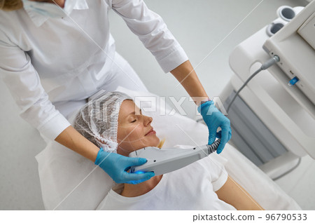 Cosmetologist applying laser to facial hair remove 96790533