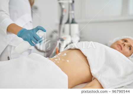 Cosmetologist putting cream on patient belly for lpg massage 96790544
