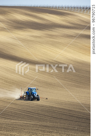 Tractor with seed drill in early spring landscape Tractor with seed drill in early spring landscape 96790715