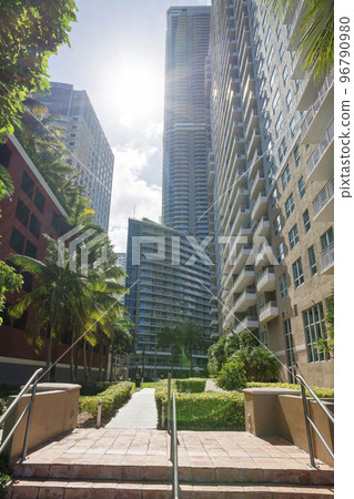 Sun behind the high-rise buildings with bushes and trees near the walkway in the middle at Miami, FL 96790980