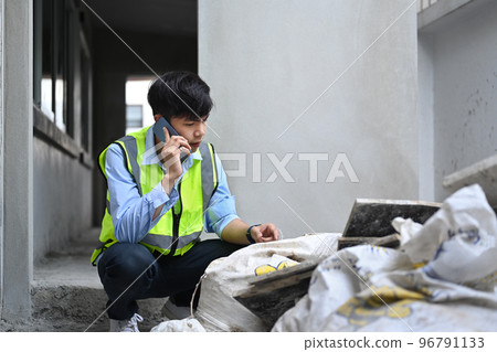 Engineer male manager wearing yellow vest talking on mobile phone under new building 96791133