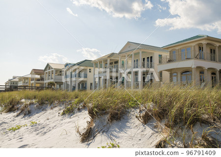 Destin, Florida- White sand dunes with grasses at the front of three-storey houses at the beach 96791409