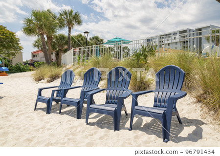 Destin, Florida- Four lounge arm chairs on a white sand near the beachgrass and fence Destin, Florida- Four lounge arm chairs on a white sand near the beachgrass and fence 96791434