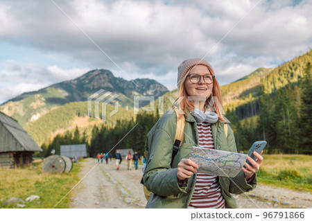 Woman hiker, searching right direction on map while taking a hiking break, having fun and relaxing while spending autumn day outdoors.  96791866