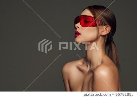 Sensual young woman with naked shoulders and well-kept skin wearing trendy red eyewear posing over dark grey background. Beauty, fashion, style 96791893