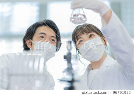 一男一女在大學實驗室裡看著燒瓶交談 96791953