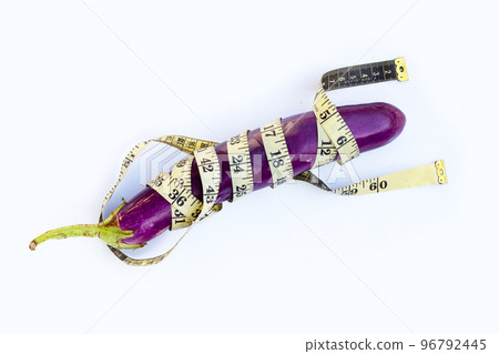 Long purple eggplant wrapped in measuring tape on white background. Long purple eggplant wrapped in measuring tape on white background. 96792445