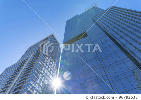 Modern glass residential buildings towering against sun and blue sky background Modern glass residential buildings towering against sun and blue sky background 96792638
