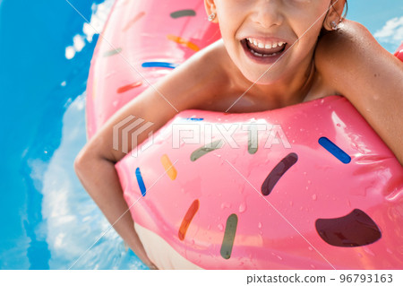 A European girl bathes in a blue pool in a pink large rubber ring. Wet hair and a happy smile. Waves, hotel and beach. The family is enjoying a happy vacation. High quality photo. A European girl bathes in a blue pool in a pink large rubber ring. Wet hair and a happy smile. Waves, hotel and beach. The family is enjoying a happy vacation. High quality photo. 96793163