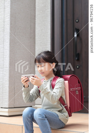 Elementary school students sitting at the entrance after school and looking at smartphones 96794156