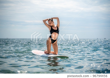 Woman sap sea. Sports girl on a surfboard in the sea on a sunny summer day. In a black bathing suit, he sits on a sapa in the sea. Rest on the sea. 96794456