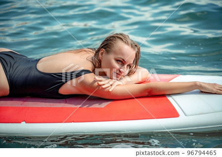Woman sap sea. Sports girl on a surfboard in the sea on a sunny summer day. In a black bathing suit, he lies on a sap in the sea. Rest on the sea. Woman sap sea. Sports girl on a surfboard in the sea on a sunny summer day. In a black bathing suit, he lies on a sap in the sea. Rest on the sea. 96794465