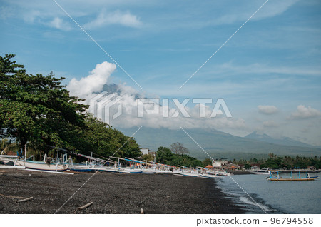 Aerial view of Amed beach in Bali, Indonesia. Traditional fishing boats called jukung on the black sand beach and Mount Agung volcano Aerial view of Amed beach in Bali, Indonesia. Traditional fishing boats called jukung on the black sand beach and Mount Agung volcano 96794558