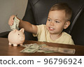 Smart happy child boy putting in piggy bank dollar banknote. Saving money in a piggy bank, learning 96796924