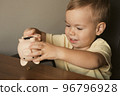 Child extract coins from piggy bank. Smart happy boy saving money in a piggy bank, learning about 96796928
