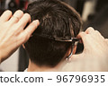 Young man getting a modern haircut. Girl hairdresser cuts a guy with scissors. Men's fashion and 96796935