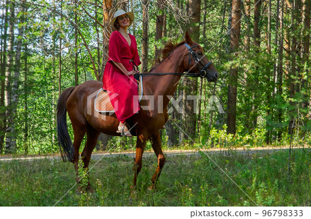 Woman in red dress rides a horse in early spring 96798333