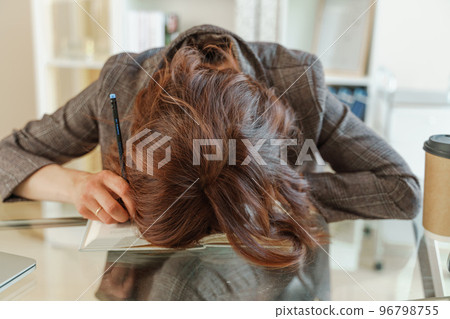 The woman is tired. Young tired woman put her head on the table, tired worker or student sitting exhausted on the table at home The woman is tired. Young tired woman put her head on the table, tired worker or student sitting exhausted on the table at home 96798755