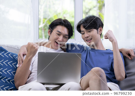 Asian gay couple using laptop in the living room. Asian gay couple using laptop in the living room. 96799230