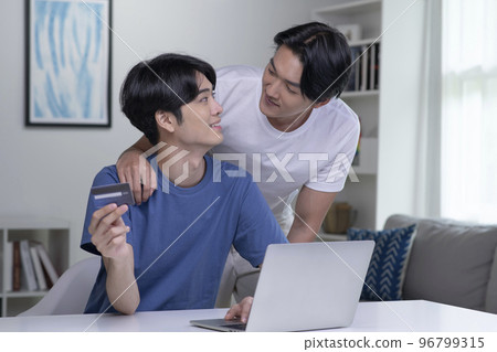 Asian gay couple holding credit card and using laptop computer Asian gay couple holding credit card and using laptop computer 96799315