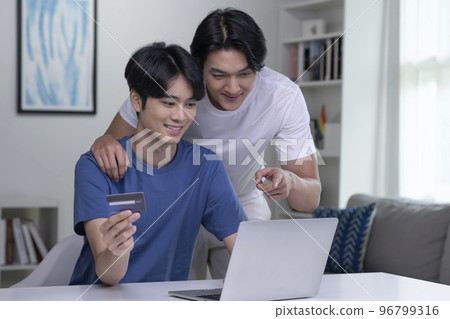 Asian gay couple holding credit card and using laptop computer Asian gay couple holding credit card and using laptop computer 96799316