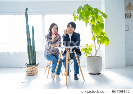 Young smiling conversational couple drinking coffee in bright living room Young smiling conversational couple drinking coffee in bright living room 96799462