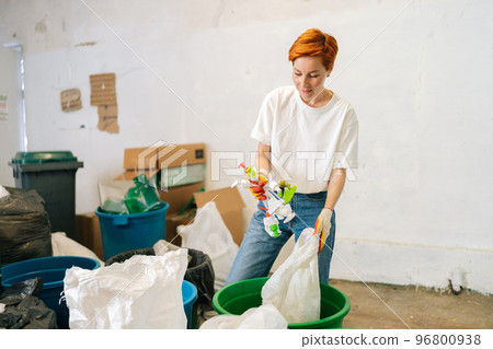 Focused young woman female worker in latex gloves sorting diverse plastic waste for further disposal at modern private waste recycling plant. Concept of environment protection and zero waste Focused young woman female worker in latex gloves sorting diverse plastic waste for further disposal at modern private waste recycling plant. Concept of environment protection and zero waste 96800938