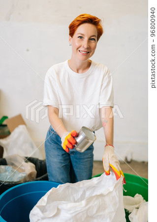 Vertical portrait of cheerful female worker in latex gloves looking at camera and sorting discarded metal cans at modern private waste recycling plant. Concept of environment protection and zero waste Vertical portrait of cheerful female worker in latex gloves looking at camera and sorting discarded metal cans at modern private waste recycling plant. Concept of environment protection and zero waste 96800940