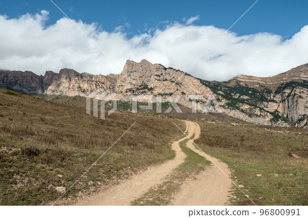 Old path through mountains. Trekking mountain trail. Bright atmospheric minimalist alpine landscape with stony footpath among grasses in highlands. Pathway uphill. Way up mountainside. Old path through mountains. Trekking mountain trail. Bright atmospheric minimalist alpine landscape with stony footpath among grasses in highlands. Pathway uphill. Way up mountainside. 96800991