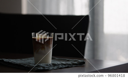 man making iced coffee with milk in thumbler glass on walnut table 96801418