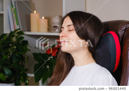 A woman sits in a chair with a massage pillow and does a neck massage. A woman sits in a chair with a massage pillow and does a neck massage. 96801440