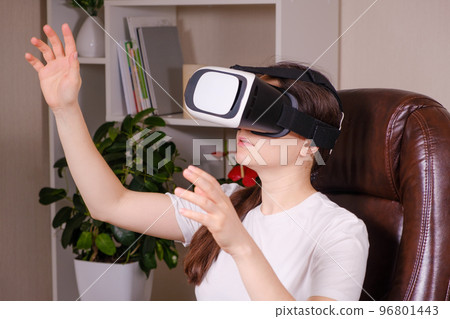 A woman in virtual reality glasses looks up against a gray background. 96801443