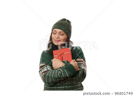 Multi-ethnic charming delightful woman in warm green Xmas patterned sweater and wool hat, gently hugging her cute present, isolated on white background with copy ad space. Boxing Day. Merry Christmas Multi-ethnic charming delightful woman in warm green Xmas patterned sweater and wool hat, gently hugging her cute present, isolated on white background with copy ad space. Boxing Day. Merry Christmas 96801749