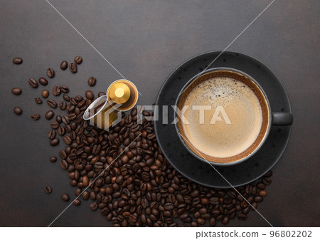 Large black coffee in porcelain cup with raw beans and capsules on brown. 96802202