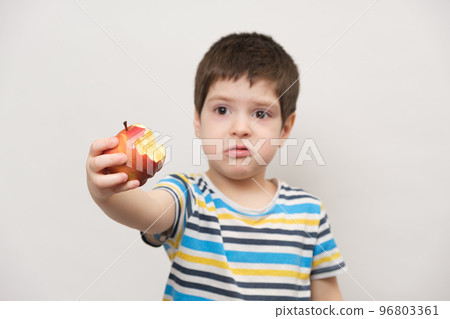 A 4 year old boy eats a red apple and squirms. The child does not like fruit A 4 year old boy eats a red apple and squirms. The child does not like fruit 96803361