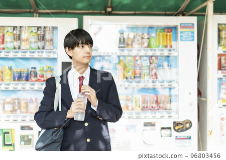 Male high school student drinking a drink in front of a vending machine Male high school student drinking a drink in front of a vending machine 96803456