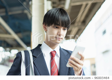 Male high school student looking at mobile phone on station platform 96803464