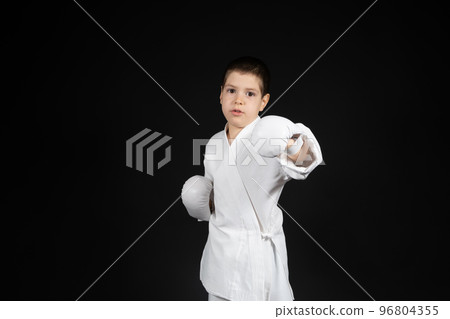 A little boy learns martial arts, doing karate in kimono and boxing gloves hand pads. 96804355