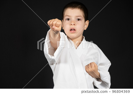 A little boy practices martial arts, karate classes in kimono on a black background, a place for text A little boy practices martial arts, karate classes in kimono on a black background, a place for text 96804369