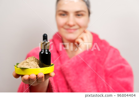 A woman keeps natural cosmetics for hair care - a bottle of oils and ubtan, a scrub of herbs A woman keeps natural cosmetics for hair care - a bottle of oils and ubtan, a scrub of herbs 96804404